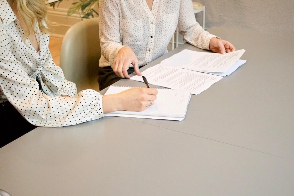 Two businesswomen going over paperwork and taking notes on an area chart